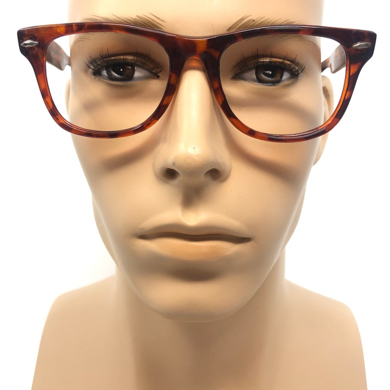 K&ouml;nnte beinhalten: Eine Brille mit Schildpattmuster und rechteckigem Rahmen. Die Brille hat ein braunes und bernsteinfarbenes Muster und wird auf einem Schaufensterkopf pr&auml;sentiert. Die Fassungen haben einen kleinen silbernen Akzent an den B&uuml;geln.