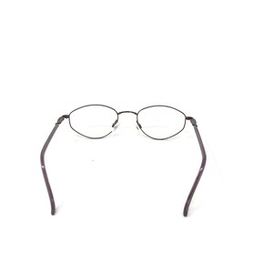 Puede incluir: Un par de gafas con montura de metal marr&oacute;n oscuro y lentes ovaladas. Las patillas son de color morado oscuro. Las gafas est&aacute;n sobre un fondo blanco.