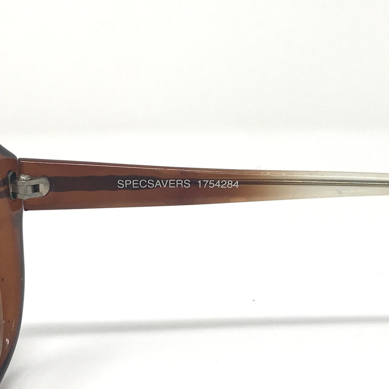 May include: Close-up of a brown and tan eyeglasses arm. The text "SPECSAVERS 1754284" is printed on the arm. The eyeglasses arm is made of a translucent material.