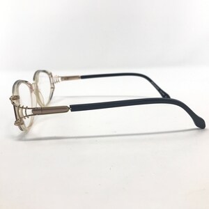 Puede incluir: Gafas con montura transparente de forma redondeada. Las monturas tienen detalles dorados y varillas negras. Las gafas est&aacute;n dise&ntilde;adas para la correcci&oacute;n de la visi&oacute;n y son adecuadas para el uso diario.