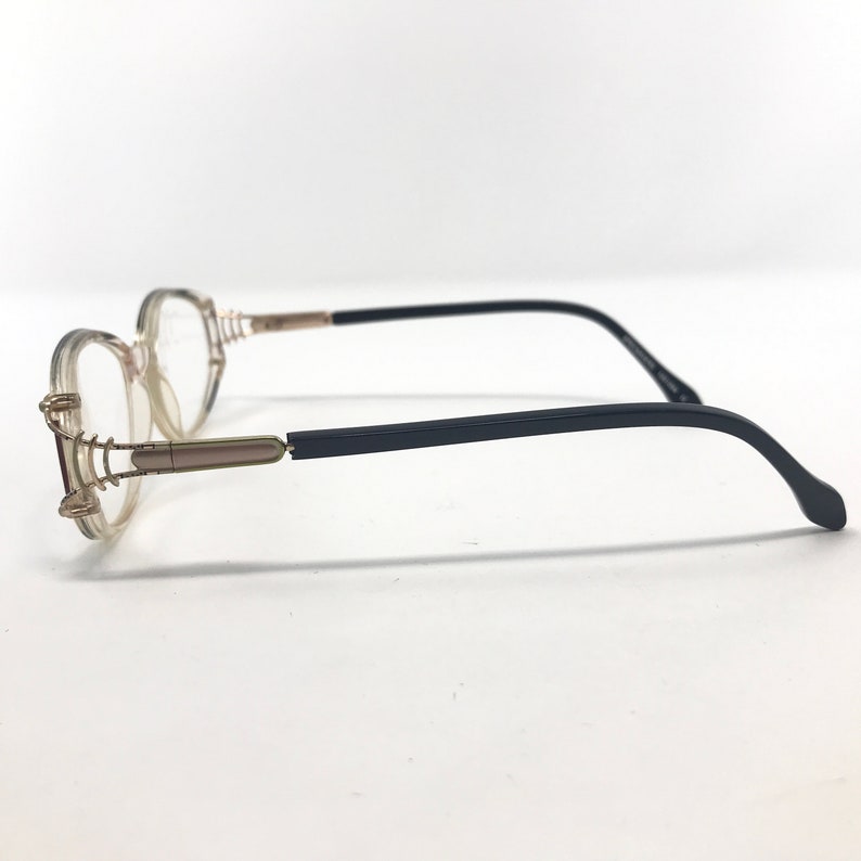 Puede incluir: Gafas con montura transparente de forma redondeada. Las monturas tienen detalles dorados y varillas negras. Las gafas est&aacute;n dise&ntilde;adas para la correcci&oacute;n de la visi&oacute;n y son adecuadas para el uso diario.