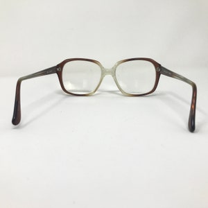 May include: Vintage eyeglasses with a brown and clear gradient frame. The rectangular lenses are set in a two-tone frame, transitioning from brown to clear. The temples are a gradient of brown and gray.
