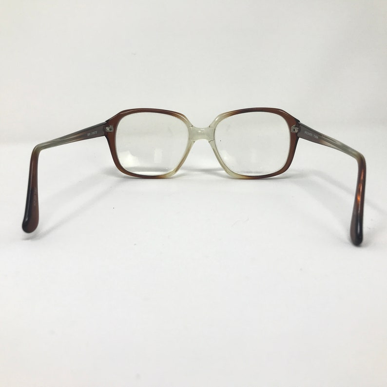 May include: Vintage eyeglasses with a brown and clear gradient frame. The rectangular lenses are set in a two-tone frame, transitioning from brown to clear. The temples are a gradient of brown and gray.