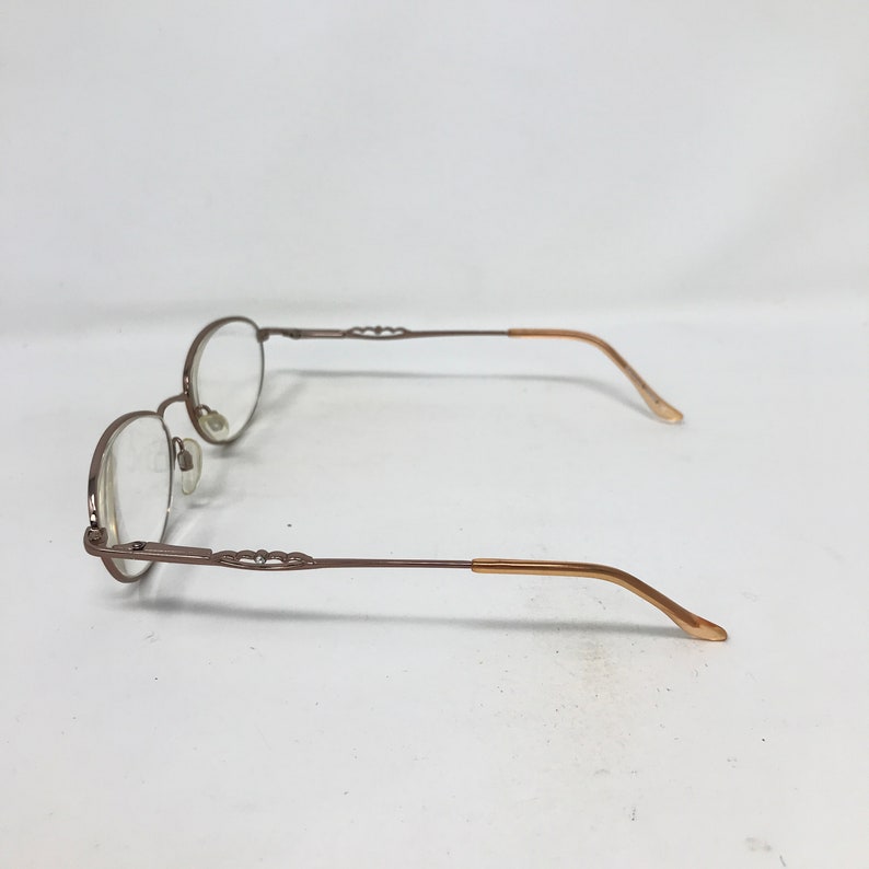Op de afbeelding: Een bril van bruin metaal met ovale glazen. De pootjes van de bril zijn in een lichtere bruine tint.