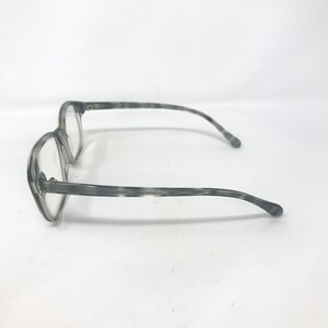 Puede incluir: Gafas grises con un patr&oacute;n veteado. Las monturas son de color gris claro y las lentes son transparentes. Las patillas de las gafas se curvan suavemente para adaptarse a las orejas. Las gafas est&aacute;n sobre un fondo blanco.