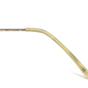 May include: Close-up of the arm of a pair of eyeglasses. The arm is a light beige color and has the text "Specsavers 1001953+ L CE" printed on it. The arm is curved and has a metal hinge.