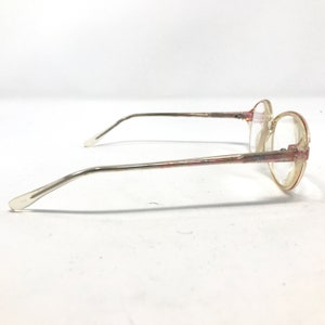 K&ouml;nnte beinhalten: Eine Brille mit ovalen, transparenten Gl&auml;sern, einem silbernen Metallrahmen und rosafarbenen Akzenten.
