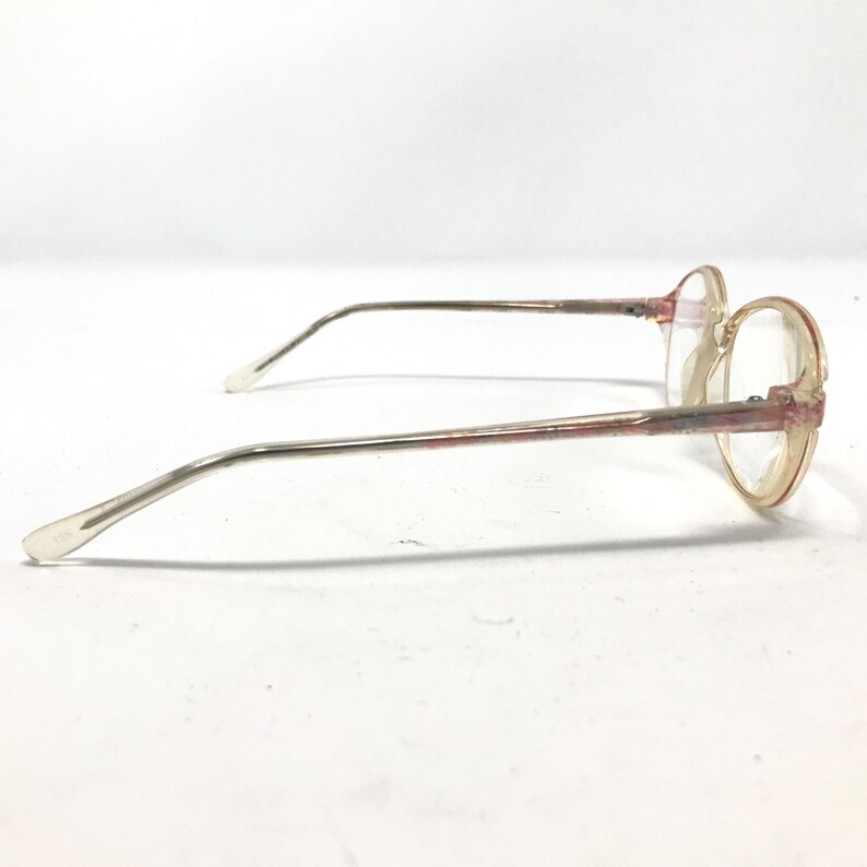 K&ouml;nnte beinhalten: Eine Brille mit ovalen, transparenten Gl&auml;sern, einem silbernen Metallrahmen und rosafarbenen Akzenten.
