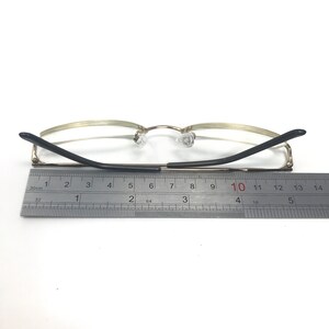 May include: Gold-tone metal eyeglasses with black arms. The arms are measured with a ruler, showing a length of 10 cm.