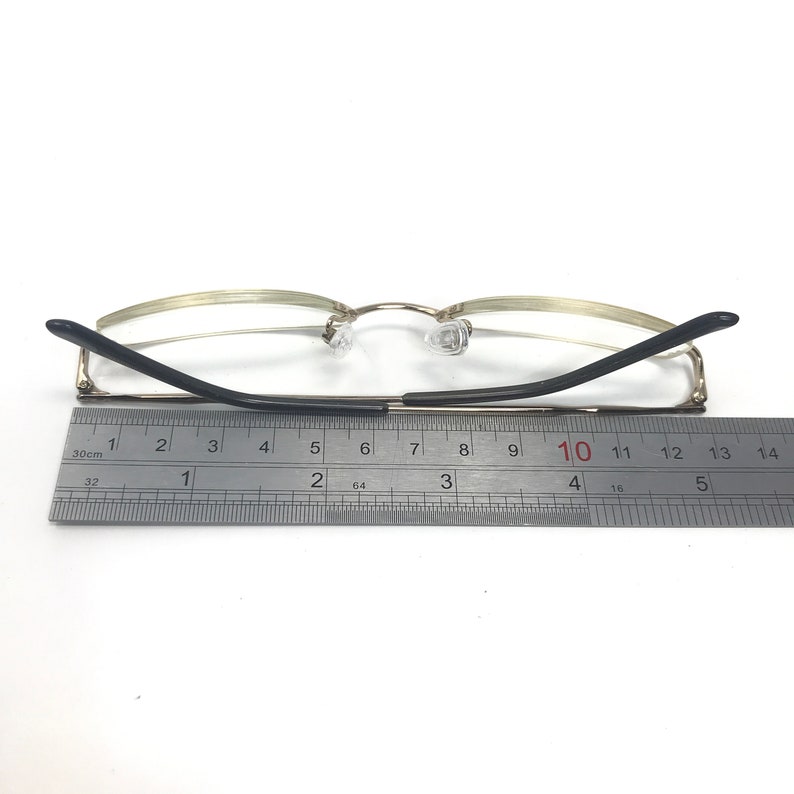 May include: Gold-tone metal eyeglasses with black arms. The arms are measured with a ruler, showing a length of 10 cm.