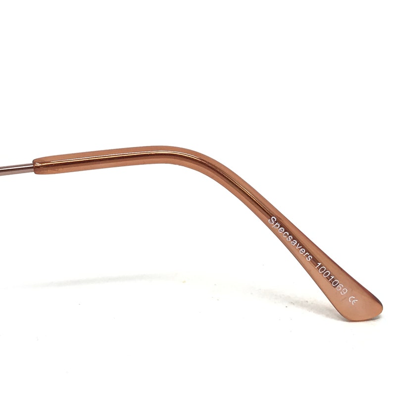 May include: Close-up of the temple arm of eyeglasses. The arm is a warm rose gold color and features the text "Specsavers 1001069 ce" printed in white. The arm curves gently and tapers towards the end.