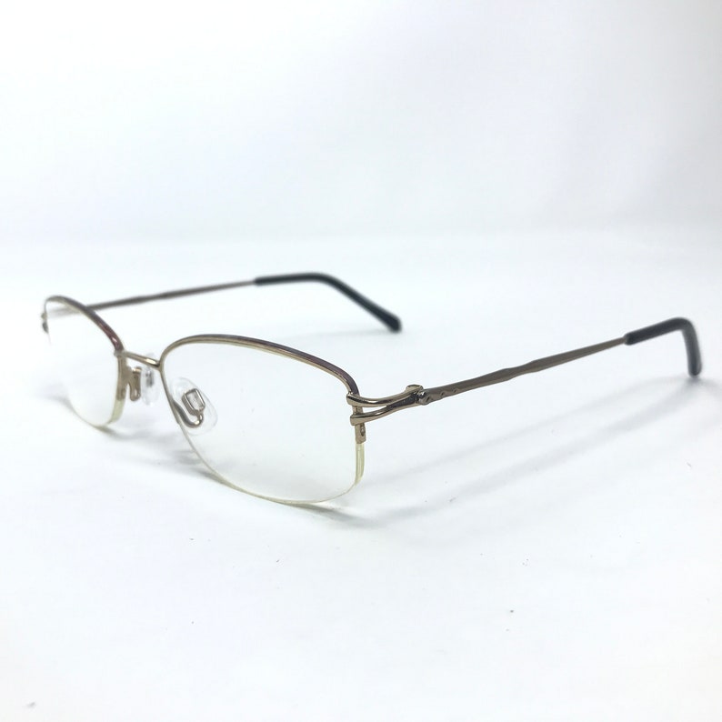 May include: A pair of gold-toned rimless eyeglasses with a thin, dark brown accent along the top of the frame.