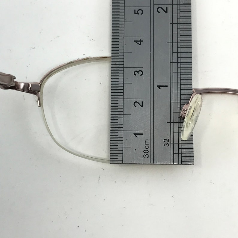 K&ouml;nnte beinhalten: Nahaufnahme einer silberfarbenen Brille mit einem transparenten Kunststoffgestell. Die Brille wird mit einem Lineal gemessen und zeigt eine L&auml;nge von 3,18 cm.