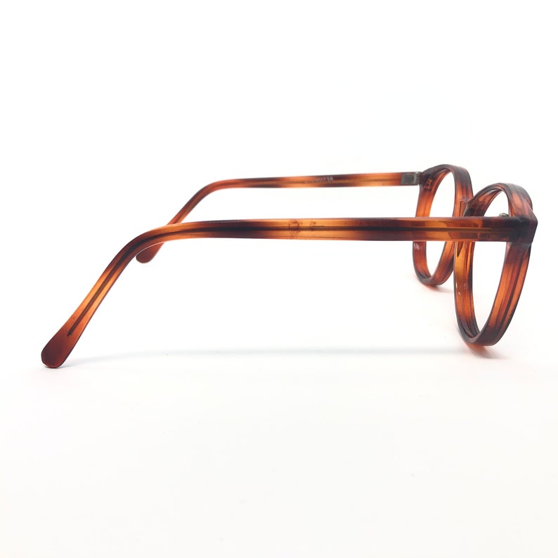 May include: A pair of eyeglasses with a brown tortoiseshell pattern. The round frames and temples are a warm brown color, with a gradient effect. The glasses are set against a white background.