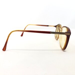 May include: Brown and gold-toned eyeglasses with a rectangular frame. The glasses have a gradient color scheme, transitioning from brown to gold on the temples. The lenses are a light yellow color.