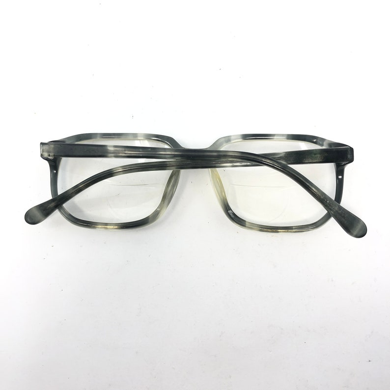 May include: Gray and white marbled eyeglasses with a rectangular frame. The glasses have clear lenses and a classic design. The temples curve gently to the ear pieces.