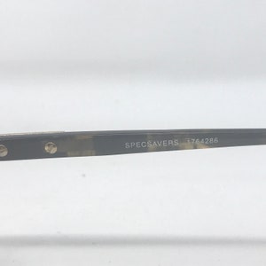 Puede incluir: Primer plano de gafas con montura oscura estampada. El texto "SPECSAVERS 1764286" est&aacute; impreso en la varilla. Las gafas est&aacute;n sobre un fondo blanco.