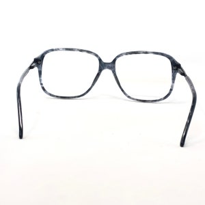 May include: Grey and white marbled eyeglasses with a square frame. The glasses have a classic design with a bridge and temples. The lenses are clear, and the frame is made of a marbled material.