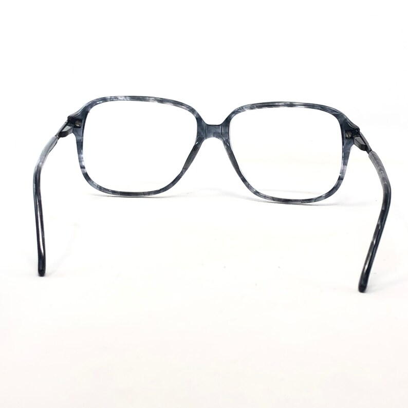 May include: Grey and white marbled eyeglasses with a square frame. The glasses have a classic design with a bridge and temples. The lenses are clear, and the frame is made of a marbled material.