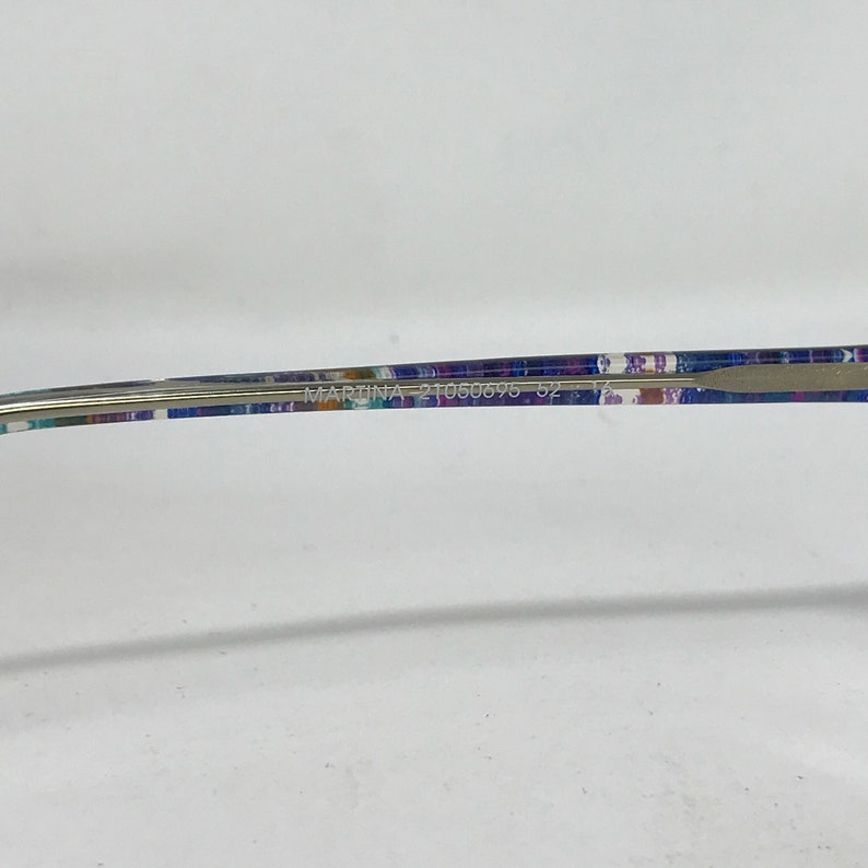 Puede incluir: Primer plano de unas gafas con un dise&ntilde;o estampado en las patillas. El texto "MARTINA 21050695 52 12" est&aacute; impreso en la patilla. La montura es plateada.