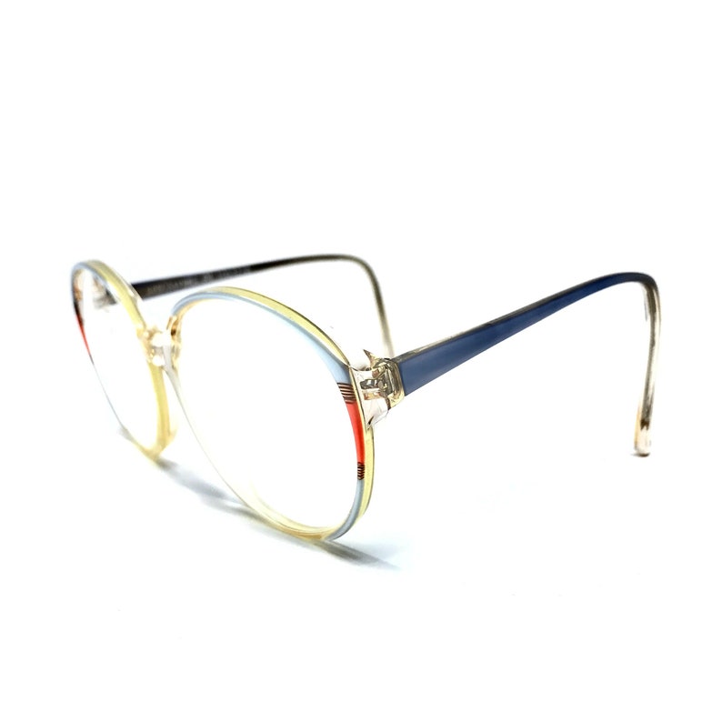 Puede incluir: Un par de gafas con un marco azul y amarillo. El marco tiene un dise&ntilde;o de rayas rojas y blancas en el lateral.