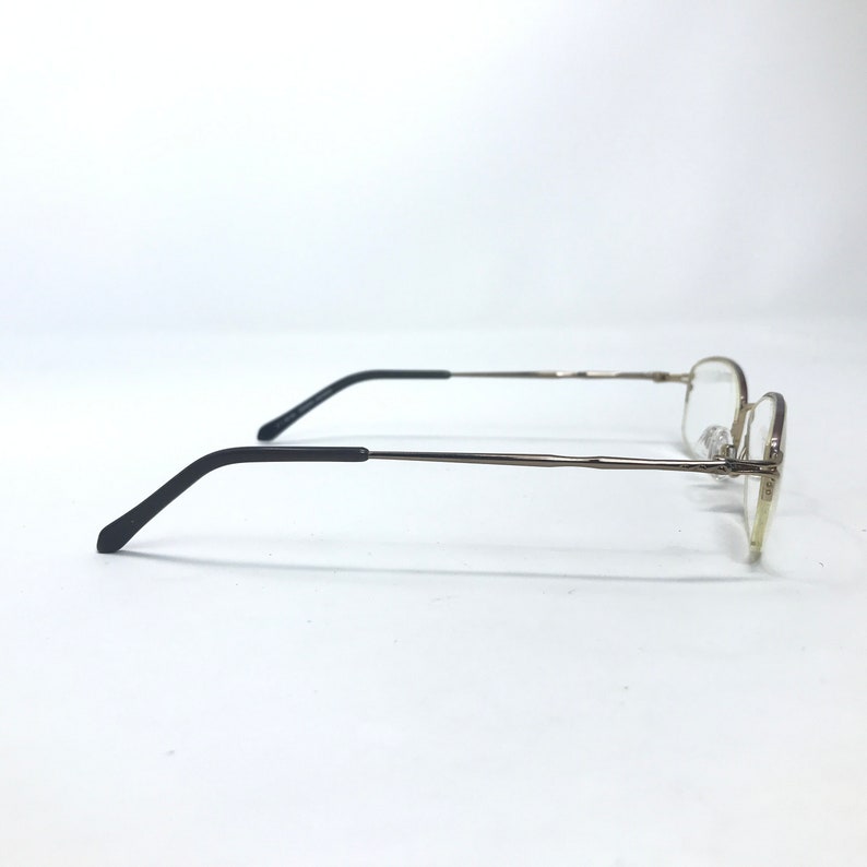 May include: Gold-tone metal eyeglasses with black plastic temple tips. The glasses have a rectangular frame and clear lenses.