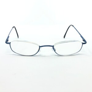 May include: A pair of rimless eyeglasses with a dark blue metal frame. The lenses are oval-shaped and clear. The temples are thin and black, and the nose bridge is a matching dark blue.
