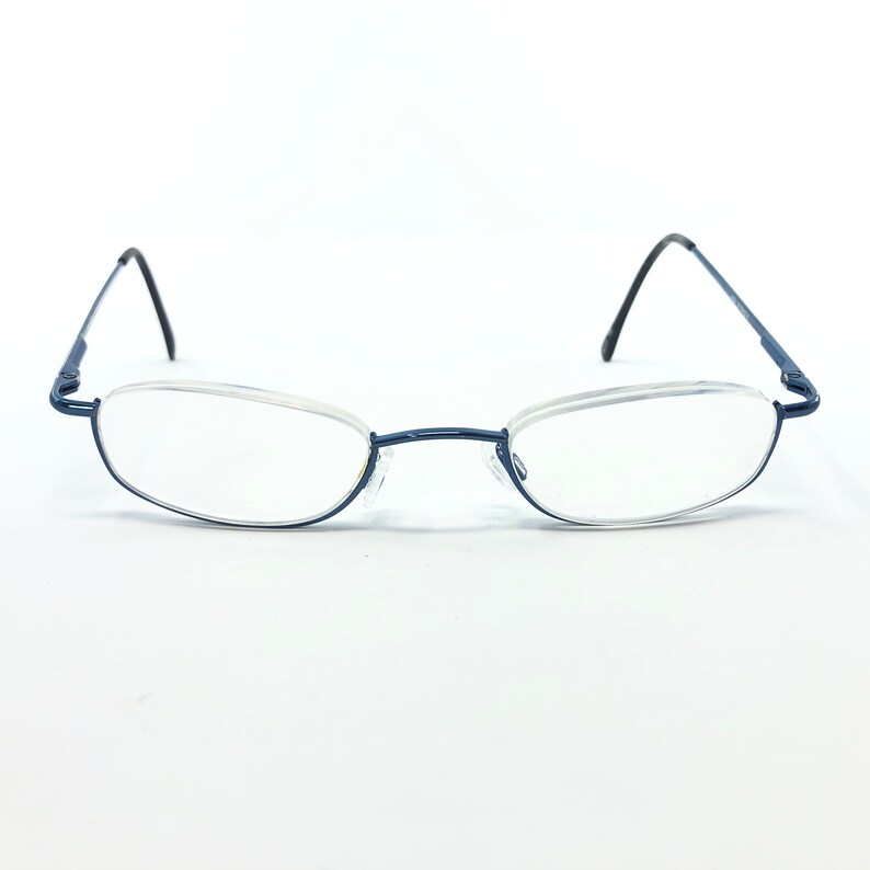 May include: A pair of rimless eyeglasses with a dark blue metal frame. The lenses are oval-shaped and clear. The temples are thin and black, and the nose bridge is a matching dark blue.