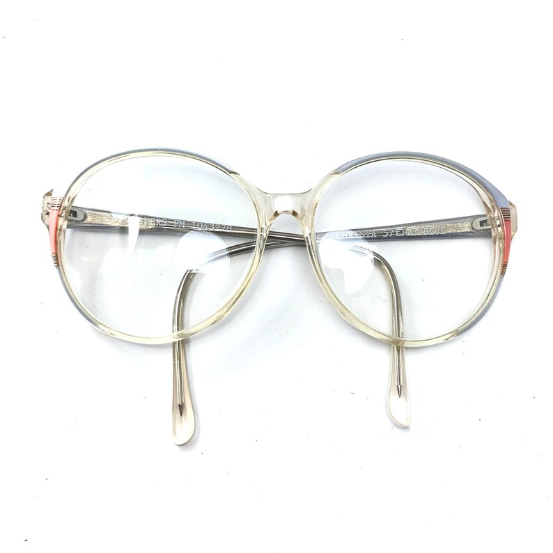 Puede incluir: Gafas de pl&aacute;stico transparente con montura azul claro y un acento rojo en el lateral. Las gafas tienen lentes redondas.