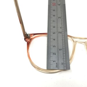 May include: Clear and light brown eyeglasses with a ruler measuring the frame. The frame is approximately 2 inches (5 cm) wide. The glasses have a classic, rectangular shape.