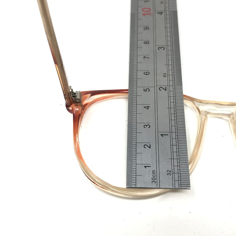 May include: Clear and light brown eyeglasses with a ruler measuring the frame. The frame is approximately 2 inches (5 cm) wide. The glasses have a classic, rectangular shape.