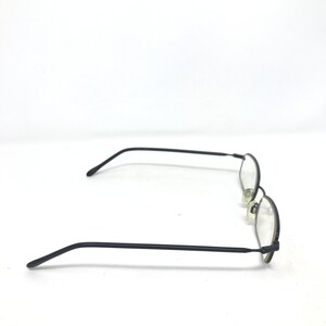 Puede incluir: Gafas negras con montura ovalada, varillas finas y almohadillas nasales. Las gafas est&aacute;n sobre un fondo blanco, mostrando el dise&ntilde;o elegante y la est&eacute;tica minimalista. Las lentes son transparentes.