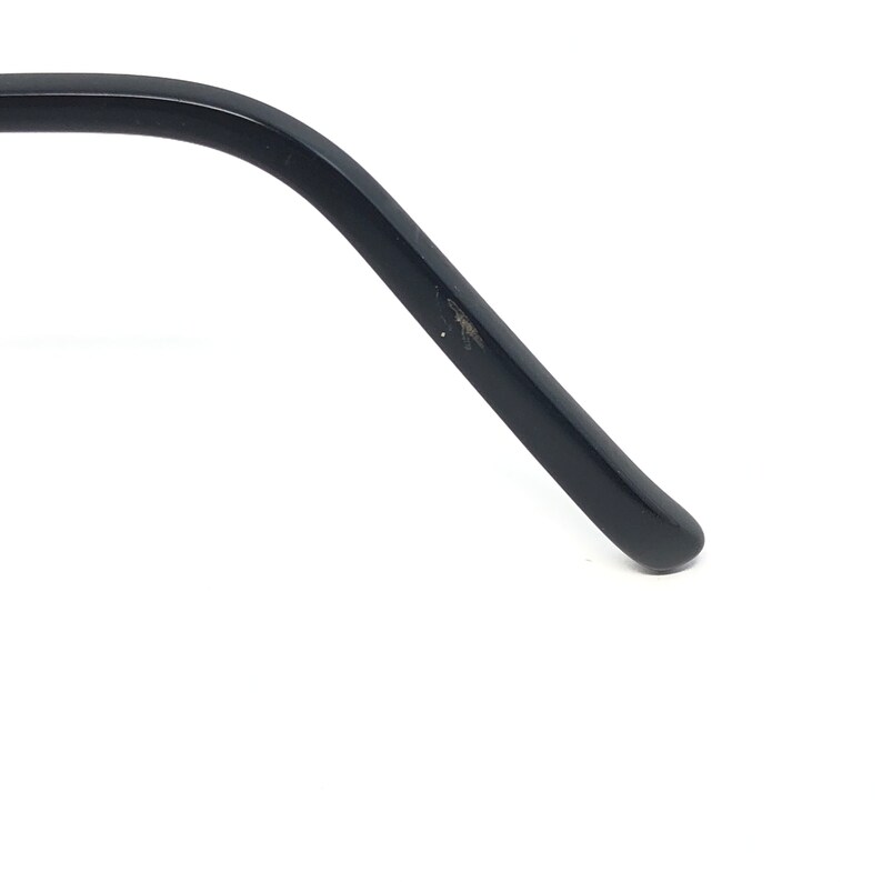 May include: Close-up of a black eyeglass arm. The arm is curved and has a rounded tip. There is a small area of wear and tear on the arm. The background is white.