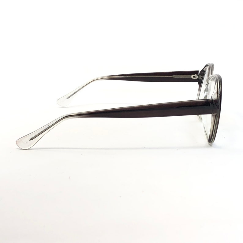 K&ouml;nnte beinhalten: Eine Brille mit einem dunkelbraunen Rahmen und klaren Gl&auml;sern. Die B&uuml;gel haben einen Farbverlauf von transparent zu dunkelbraun. Die Brille ist vor einem wei&szlig;en Hintergrund platziert.