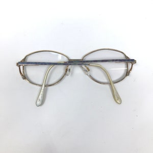 Op de afbeelding: Een bril met een goudkleurig metalen montuur en heldere glazen. De bril heeft een rechthoekige vorm met afgeronde randen. De veren zijn licht goudkleurig en de neuspads zijn transparant.