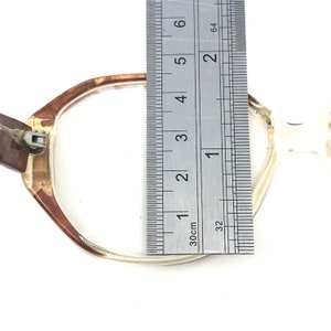 May include: Clear eyeglasses with a brown and clear frame. The glasses are measured with a ruler, showing a width of approximately 2 inches. The glasses are on a white background.