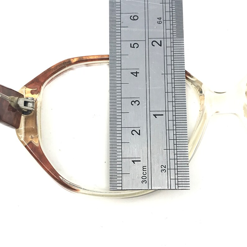 May include: Clear eyeglasses with a brown and clear frame. The glasses are measured with a ruler, showing a width of approximately 2 inches. The glasses are on a white background.