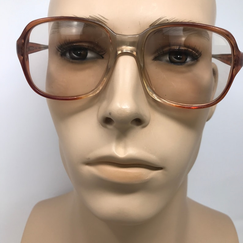 May include: Vintage eyeglasses with a clear, rectangular frame and brown gradient lenses. The frames have a light brown color with a darker brown accent on the edges. The glasses are displayed on a mannequin head.