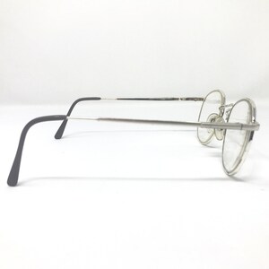 Peut inclure: Lunettes &agrave; monture argent&eacute;e avec verres ronds. Les lunettes ont une fine monture argent&eacute;e et des branches noires. Les verres sont clairs. Les lunettes sont pos&eacute;es sur un fond blanc.