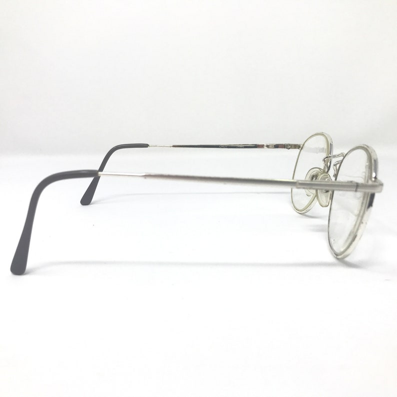 Peut inclure: Lunettes &agrave; monture argent&eacute;e avec verres ronds. Les lunettes ont une fine monture argent&eacute;e et des branches noires. Les verres sont clairs. Les lunettes sont pos&eacute;es sur un fond blanc.