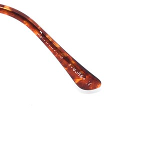 May include: Close-up of the temple arm of eyeglasses with a tortoiseshell pattern. The arm has the text "Spectacles" and the numbers "570366+". The arm is brown and tan.