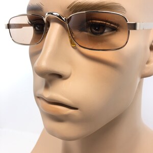 May include: Gold-toned rectangular sunglasses with gradient brown lenses. The glasses have a thin metal frame and a curved bridge. The temples are straight and extend to the ears. The sunglasses are displayed on a mannequin head.