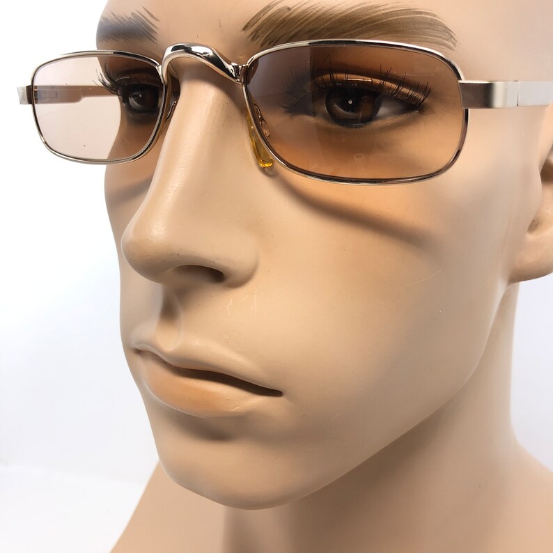 May include: Gold-toned rectangular sunglasses with gradient brown lenses. The glasses have a thin metal frame and a curved bridge. The temples are straight and extend to the ears. The sunglasses are displayed on a mannequin head.