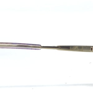 May include: Close-up of eyeglasses with a silver metal frame and purple temples. The glasses have a sleek, modern design, with a focus on the details of the frame and the temples. The image is set against a white background.