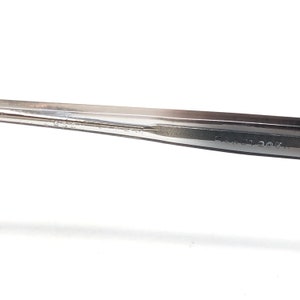 Op de afbeelding: Close-up van een zilveren metalen gereedschap met de tekst "EASY LOOK" op de zijkant. Het gereedschap heeft een puntig uiteinde en een plat, langwerpig lichaam. De achtergrond is wit.