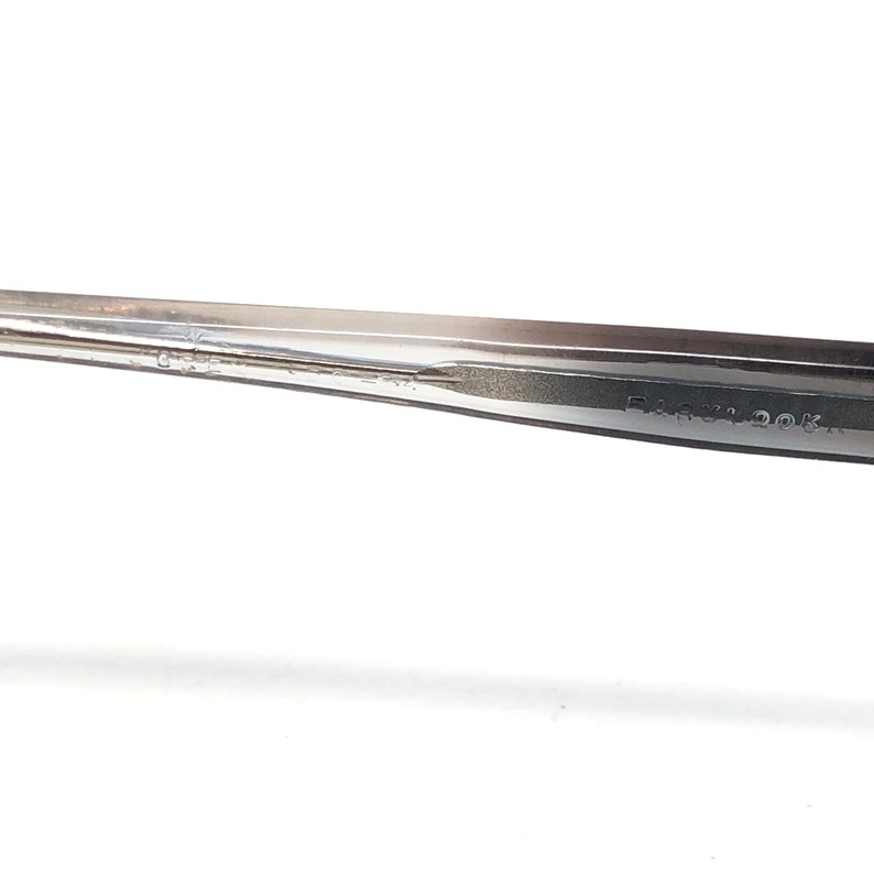 Op de afbeelding: Close-up van een zilveren metalen gereedschap met de tekst "EASY LOOK" op de zijkant. Het gereedschap heeft een puntig uiteinde en een plat, langwerpig lichaam. De achtergrond is wit.