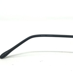 Puede incluir: Primer plano de una patilla de gafas negra. El brazo se curva suavemente y tiene los n&uacute;meros "90 20" impresos en el extremo. El texto "RAOUL 47005913" est&aacute; impreso en el brazo.