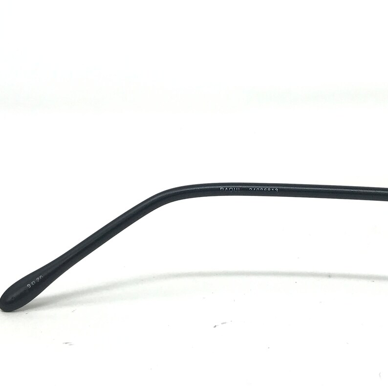 Puede incluir: Primer plano de una patilla de gafas negra. El brazo se curva suavemente y tiene los n&uacute;meros "90 20" impresos en el extremo. El texto "RAOUL 47005913" est&aacute; impreso en el brazo.