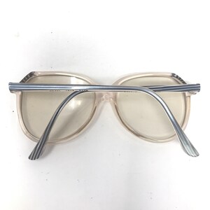 May include: Clear-framed eyeglasses with a light blue and white striped design on the temples and top bar. The lenses are a light tint, and the frame has a rounded, rectangular shape. The glasses are viewed from the back.