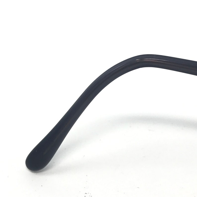 May include: Close-up of a black eyeglass arm. The arm curves gently and ends in a rounded tip. The surface appears smooth and glossy, with a slight reflection.